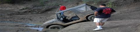 1986 Ford Bronco - A Jeep is stuck in thick mud, with two individuals observing the situation.