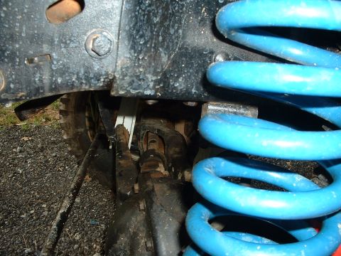 1985 Ford Bronco - Low-angle close-up under the front of a lifted 4x4, showing a bright blue lift coil spring seated on the axle perch alongside the radius ar…