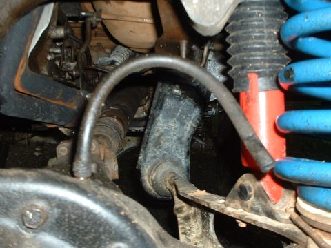 1985 Ford Bronco - Close-up inside the front suspension of a lifted 4x4, showing a red-bodied shock with a black rubber boot next to a blue lift coil spring a…