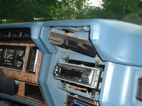 1985 Ford Bronco - Interior shot of a light-blue 1980s Ford dash with woodgrain instrument bezel, showing the analog speedometer and gauge cluster at left and…