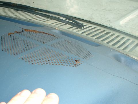 1985 Ford Bronco - Close-up of a blue vinyl dash pad photographed from inside the cab, showing a long crack along the top and the perforated defroster speaker…