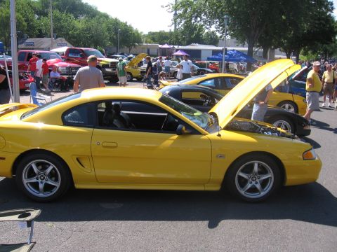 1989 Ford Mustang - A yellow coupe, likely a 1994 Ford Mustang, is displayed with its hood open at an outdoor car show.