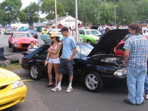 1989 Ford Mustang - A black Fox-body Ford Mustang LX 5.0 hatchback displayed hood-up at a crowded outdoor car show, sitting on silver pony-style wheels with 5.…