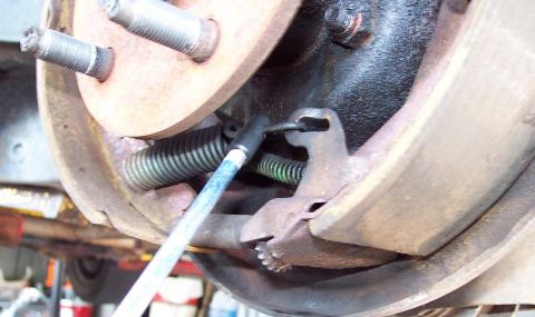 1985 Ford LTD Crown Victoria - Close-up of a rear drum brake with the drum off, showing the backing plate, wheel studs, a brake shoe, the star-wheel adjuster spring and t…