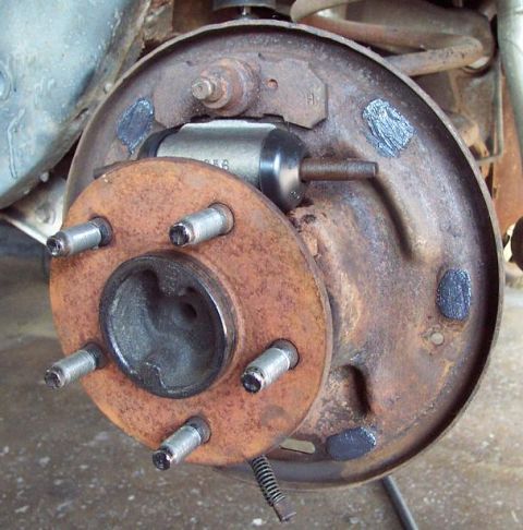 1985 Ford LTD Crown Victoria - A rear drum brake with the drum pulled off, exposing a rusty five-lug axle flange with new-looking wheel studs, the wheel cylinder with its…