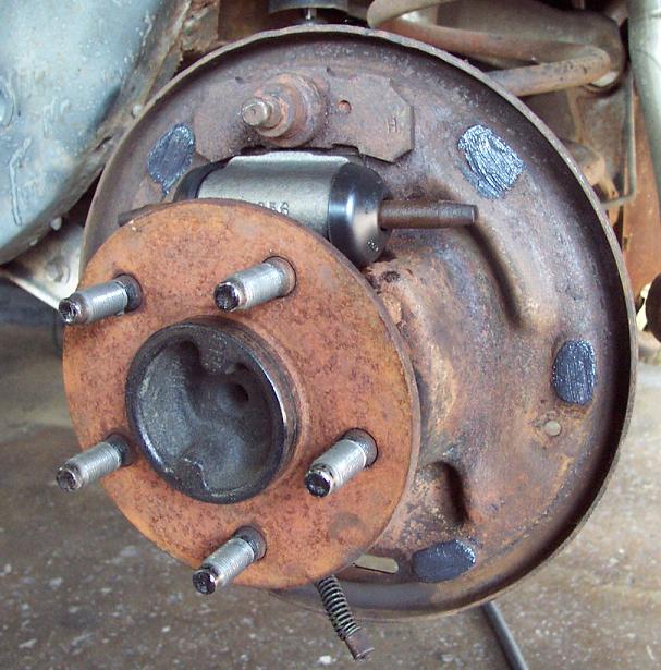 Rear drum brake with drum removed showing rusty five-lug axle flange and wheel cylinder