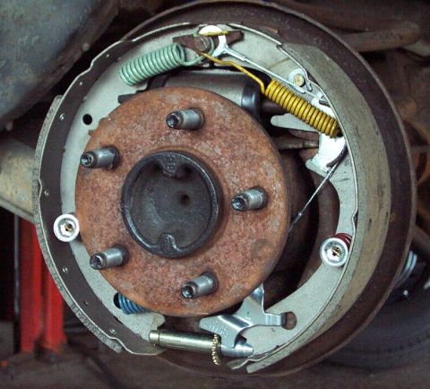 1985 Ford LTD Crown Victoria - Close-up of a disassembled rear drum brake with the drum removed, showing a rusty hub with five wheel studs, brake shoes, return springs (g…