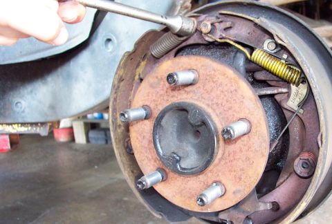 1985 Ford LTD Crown Victoria - Close-up of a rusty rear brake hub with five wheel studs and exposed drum brake components, including the yellow return spring and backing…