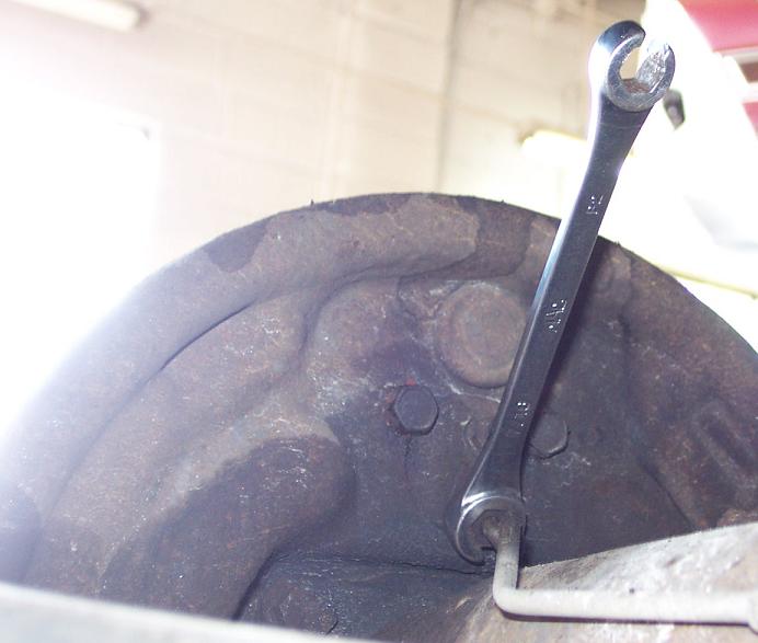Wrench on a brake line fitting at a rusty round backing plate under a vehicle