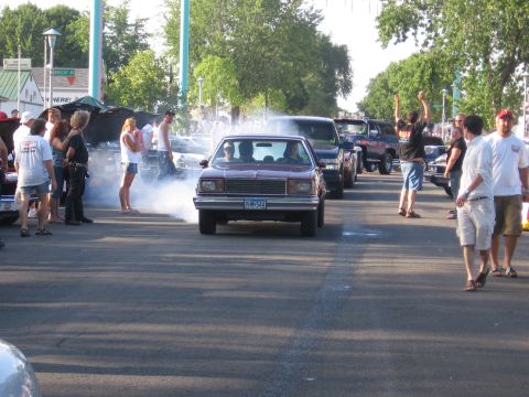 1989 Ford Mustang - A maroon sedan performs a burnout, surrounded by onlookers and other vehicles.