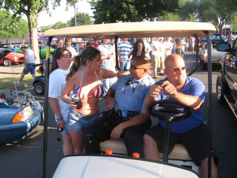 1989 Ford Mustang - A group of people are in a golf cart at an outdoor gathering, with a blue car visible in the background.