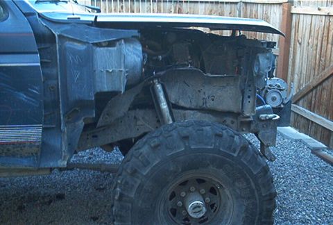 1986 Ford Bronco - The front fender of a dark blue Ford Bronco is removed, revealing the engine compartment and a large off-road tire.