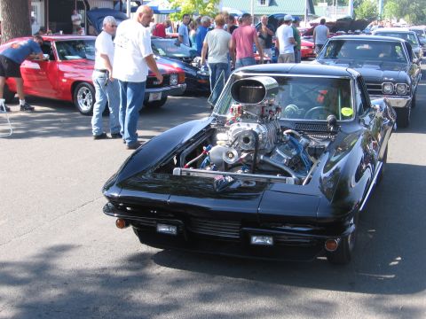1989 Ford Mustang - A heavily modified black car with a prominent supercharger is displayed outdoors among other vehicles and spectators.