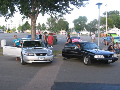 1989 Ford Mustang - Two Ford Mustangs, a silver 1999 model and a black 1989 model, are parked side-by-side in an outdoor lot.