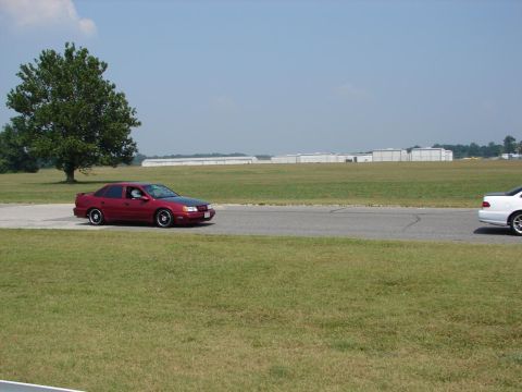 1992 Ford Taurus - A red 1992 Ford Taurus is seen on a track, with another vehicle visible to the right.