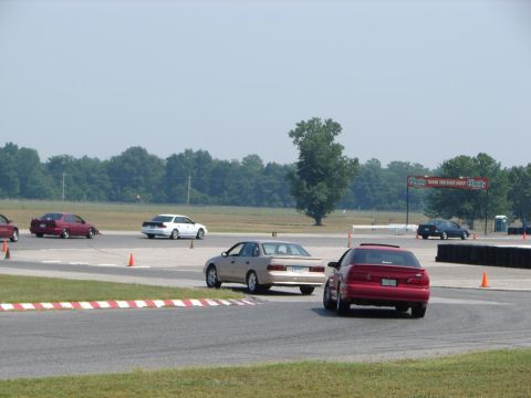 1992 Ford Taurus - A red 1992 Ford Taurus navigates a turn on a race track, with other vehicles visible in the background.