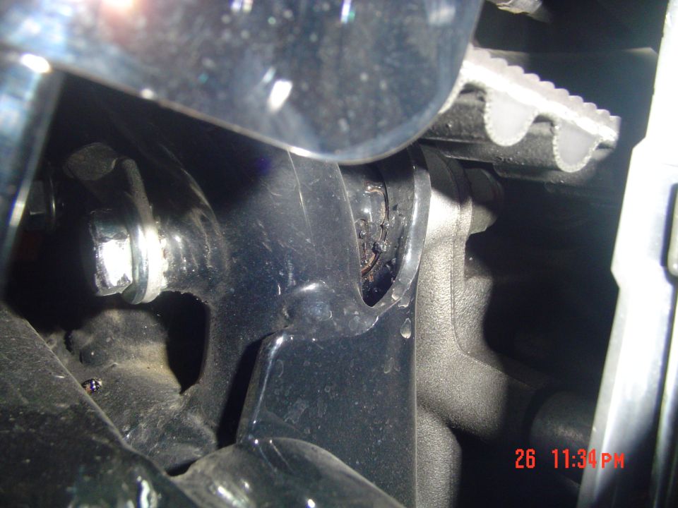 Close-up under-hood shot of wet engine area with silver bolt, serpentine belt and cast bracket, date stamp