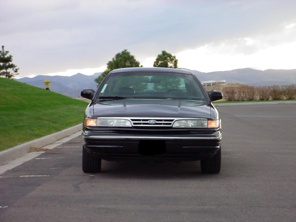 Front view of a black sedan parked on asphalt with a grassy hill and mountains in the background