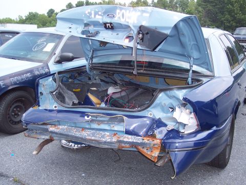 1991 Ford LTD Crown Victoria - This damaged police car shows significant rear-end collision damage, with the trunk open and wiring exposed.