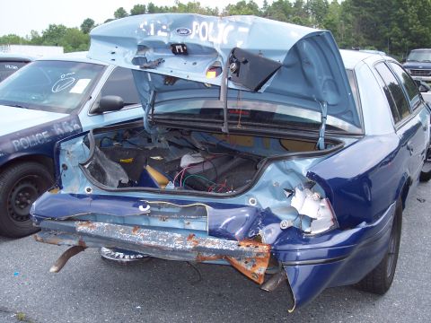 1991 Ford LTD Crown Victoria - Damaged police car with trunk open, showing extensive rear-end damage. Another police car is parked alongside.