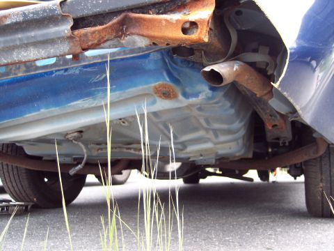 1991 Ford LTD Crown Victoria - The underside of a blue vehicle displays significant rust and a portion of the exhaust system.