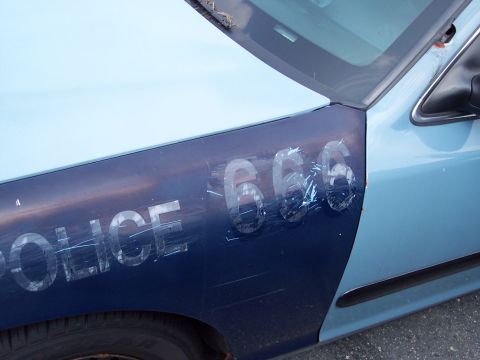 1991 Ford LTD Crown Victoria - Close-up of a police car's fender showing the word 'POLICE' and the number '666' with significant damage.