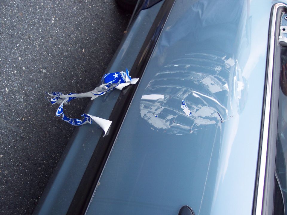 Close-up of a car door showing damaged paint and a torn blue and white star decal