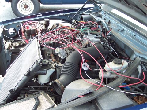 1991 Ford LTD Crown Victoria - The engine bay is filled with a chaotic mess of wires, with the radiator disconnected. A portion of another vehicle is visible in the backg…