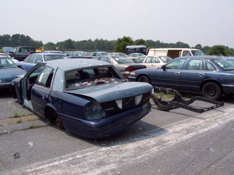 1991 Ford LTD Crown Victoria - A damaged 1991 Ford Crown Victoria LTD sits in a junkyard with other vehicles.