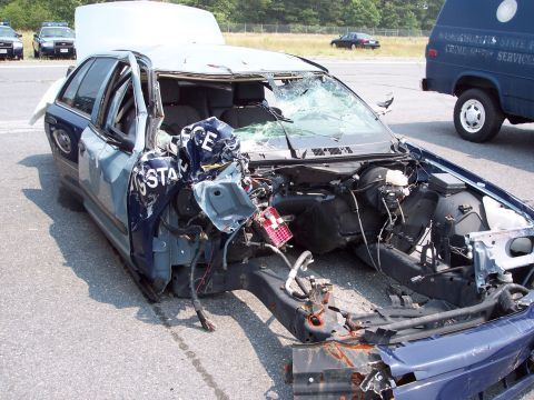 1991 Ford LTD Crown Victoria - A heavily damaged police car sits on pavement, with other vehicles and a van in the background.