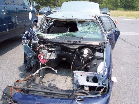 1991 Ford LTD Crown Victoria - A severely damaged blue sedan sits in a lot, its front end missing and windshield broken.