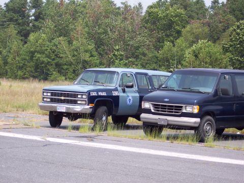 1991 Ford LTD Crown Victoria - Two police vehicles, a Chevrolet Suburban and a Ford van, are parked next to each other.