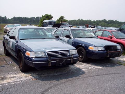 1991 Ford LTD Crown Victoria - Two police-style sedans are parked in an outdoor lot, with other vehicles visible in the background.
