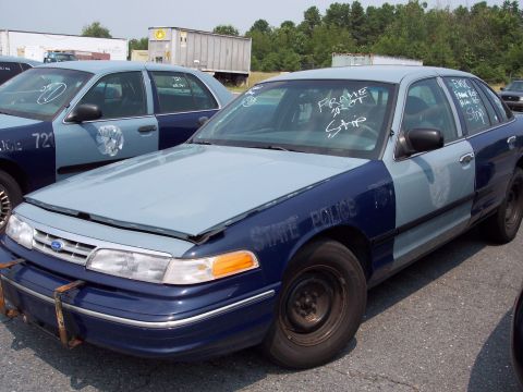 1991 Ford LTD Crown Victoria - Two Ford Crown Victoria police cars are parked in a lot, one with "STATE POLICE" visible on its fender.