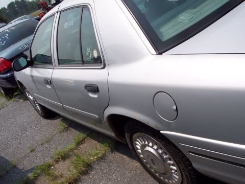 1991 Ford LTD Crown Victoria - A silver sedan is parked in a lot with other vehicles. Text is visible on the rear window.