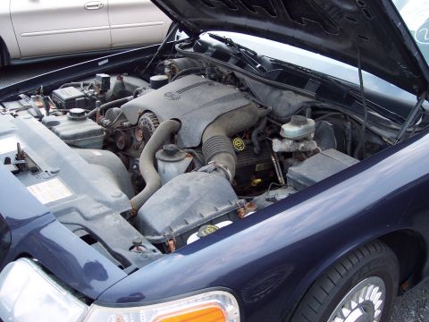 1991 Ford LTD Crown Victoria - The engine bay of a dark blue Ford Crown Victoria is open, revealing the engine components. Another vehicle is visible in the background.