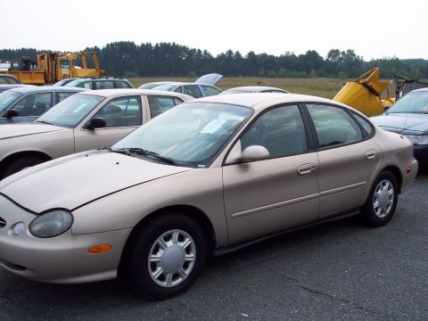 1991 Ford LTD Crown Victoria - A tan sedan is parked in a lot with other vehicles, showing its side profile and a slightly damaged front end.