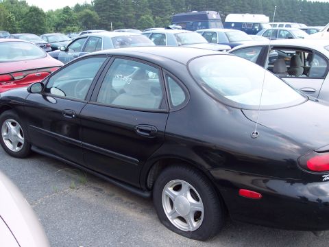 1991 Ford LTD Crown Victoria - A black sedan with a flat tire is parked in a lot full of other vehicles.