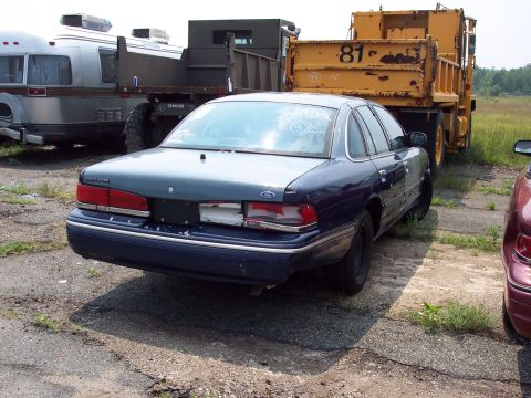 1991 Ford LTD Crown Victoria - A dark blue sedan sits parked in a lot with a large yellow dump truck behind it.