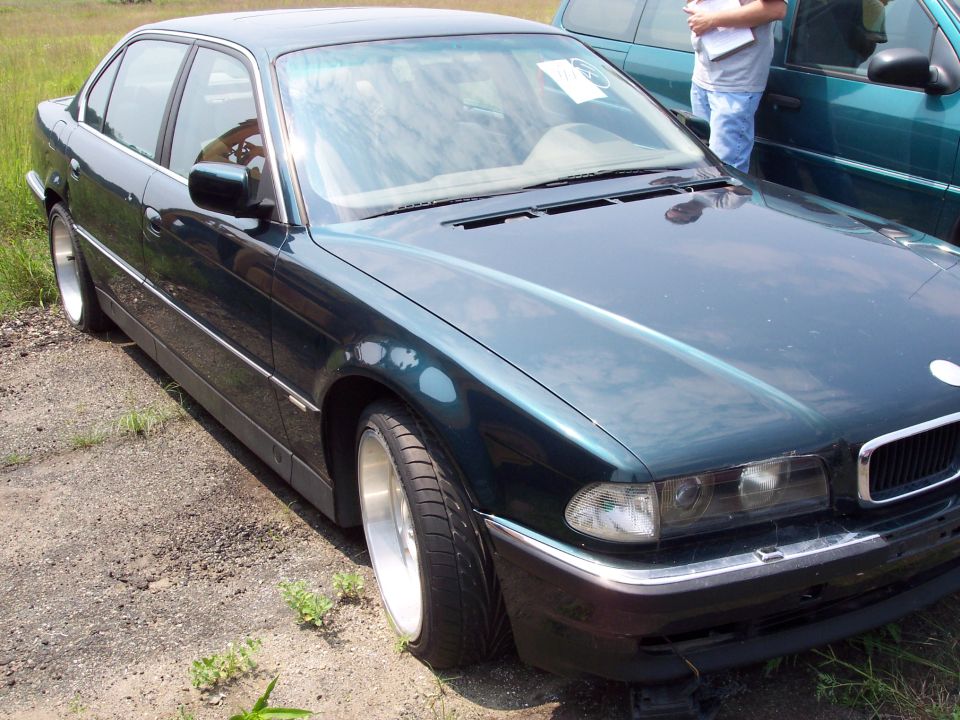Dark green sedan, 3/4 front view. Another vehicle is partially visible behind it
