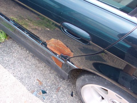 1991 Ford LTD Crown Victoria - Rust is actively flaking off the lower body panels of this dark green vehicle.