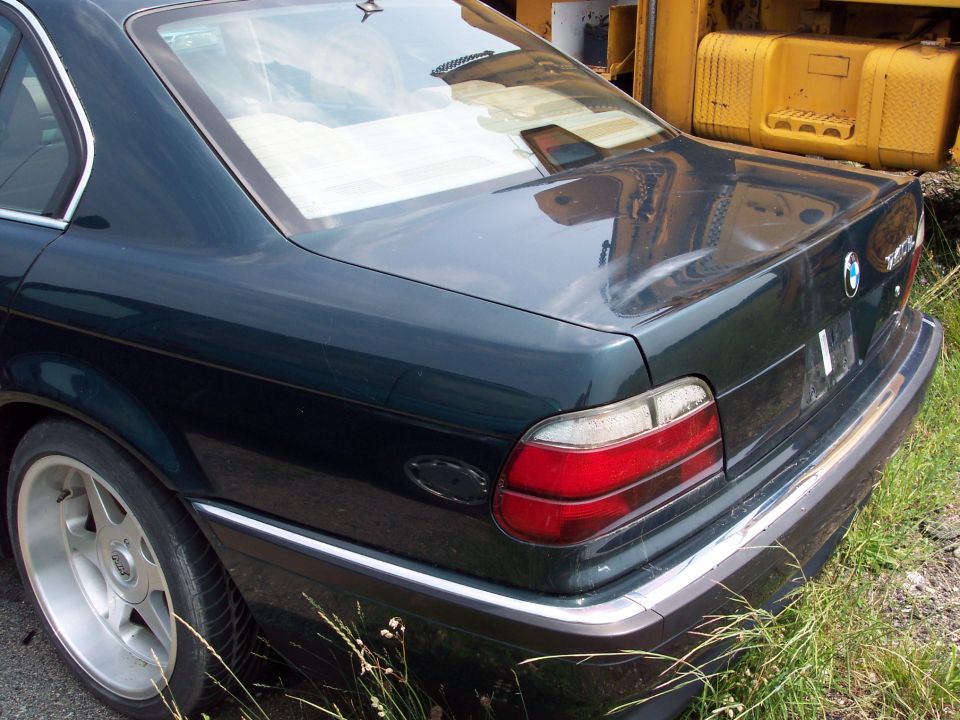 Dark sedan's rear quarter panel and trunk. Yellow construction equipment is behind it
