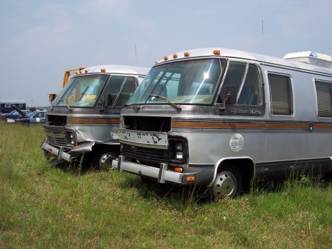 1991 Ford LTD Crown Victoria - Two motorhomes sit in a field under a cloudy sky, with one showing significant front-end damage.