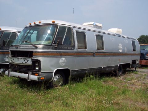 1991 Ford LTD Crown Victoria - This Airstream 325 motorhome is seen from a 3/4 front angle, with its front grille missing and parked in overgrown grass.