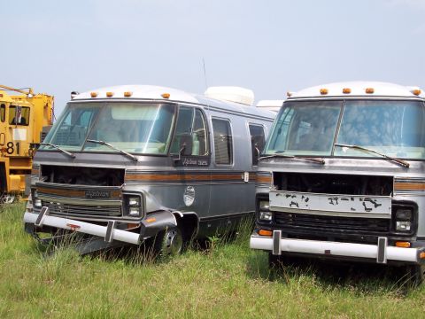 1991 Ford LTD Crown Victoria - Two abandoned RVs sit in a field under a clear sky.