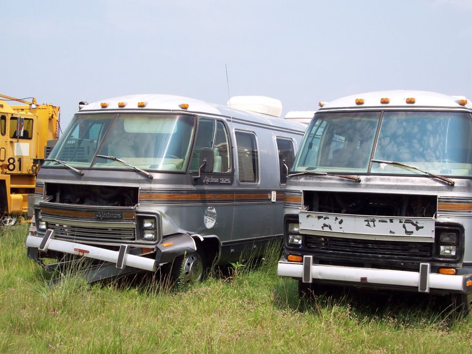 Two older model RVs parked in a grassy field, front ends visible