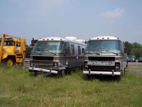 1991 Ford LTD Crown Victoria - Two older RVs sit in a field with construction equipment nearby under a partly cloudy sky.