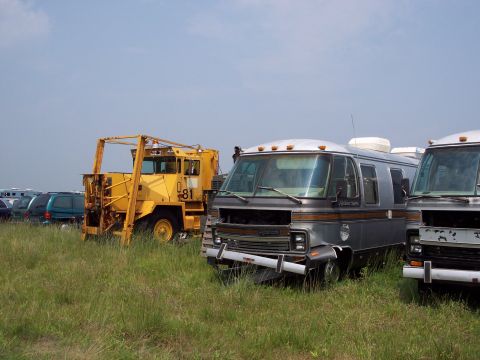 1991 Ford LTD Crown Victoria - Multiple vehicles, including a motorhome and a yellow industrial vehicle, sit in a field under a clear sky.
