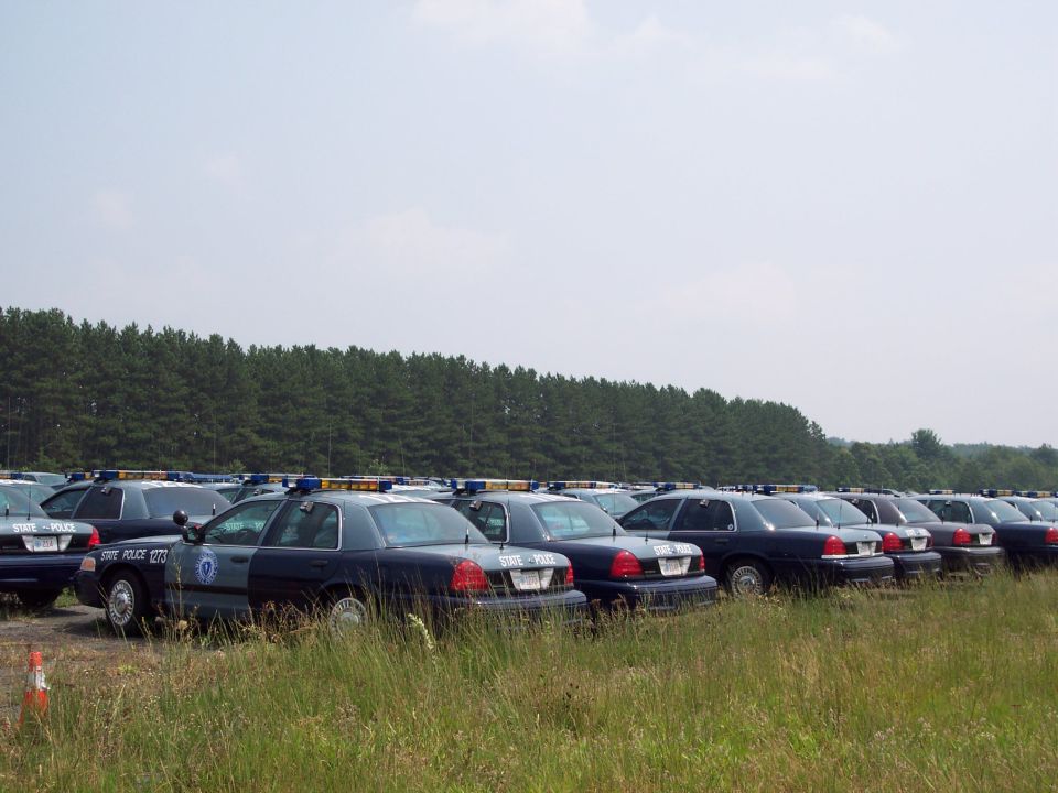 Fleet of dark blue police cars parked in a field, side view