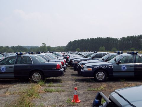 1991 Ford LTD Crown Victoria - A fleet of police sedans, likely Ford Crown Victorias, are parked in rows under a cloudy sky.